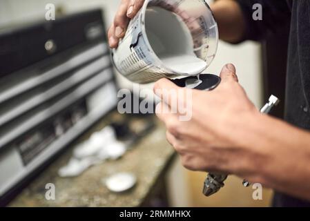 Die Hände eines jungen, nicht wiedererkennbaren Mannes, der in seiner Werkstatt Farbe in eine Spritzpistole gießt. Nahaufnahme. Stockfoto