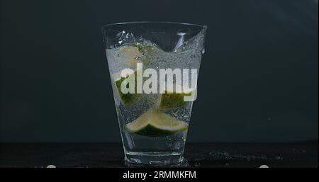 Grüne Zitrusfrüchte, Zitrusfrüchte aurantifolia, fallen in ein Glas Wasser, Stockfoto