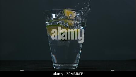 Grüne Zitrusfrüchte, Zitrusfrüchte aurantifolia, fallen in ein Glas Wasser, Stockfoto