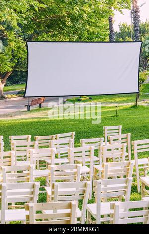 Open-Air-Kino: Eine leere weiße Leinwand wartet auf die Projektion in einem Park, der im Sommer Unterhaltung im Freien und Filmmagie verspricht. Stockfoto