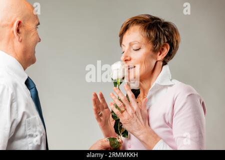 Diese weiße Rose riecht köstlich, der Duft unserer Liebe, mein Schatz. Wir haben uns schon so lange geliebt, und doch scheint es wie gestern. Älterer Mann Stockfoto