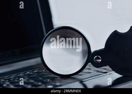 Laptop-Computer mit Tastatur und Lupe auf der Oberseite, die den Suchvorgang im Internet darstellt und alte und neue Konzepte kombiniert Stockfoto