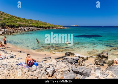 Menschenmassen von Einheimischen und Touristen an einem kleinen, felsigen Strand umgeben von klarem, türkisfarbenem Wasser auf Kolokitha, Elounda, Kreta Stockfoto