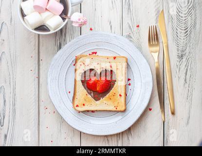 Herzförmiges geröstetes Brot mit Nutella und frischer Erdbeere auf Holztisch Stockfoto