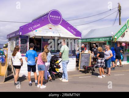 Eiskiosk UK; Leute, die an einem sonnigen Sommertag in West Bay, Dorset England, in der Warteschlange stehen, um Eis zu kaufen. Englischer Lebensstil im Urlaub. Stockfoto