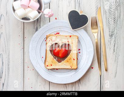 Herzförmiges geröstetes Brot mit Nutella und frischer Erdbeere auf Holztisch Stockfoto