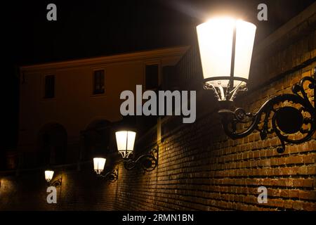 Beleuchtete Straßenlaternen an einer Ziegelmauer in der Nacht Stockfoto