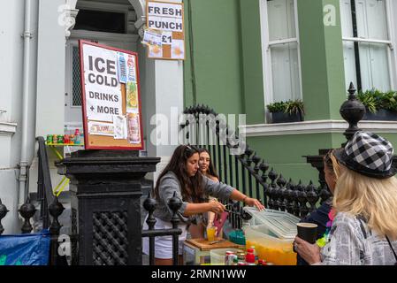 Frauen, die Getränke von der Vorderseite eines Hotels bei der Notting Hill Carnival Grand Parade 2023, London, Großbritannien, verkaufen. Frischer Punsch Stockfoto