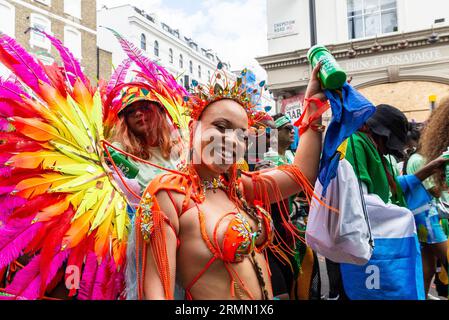 Teilnehmerin bei der Notting Hill Carnival Grand Parade 2023 in London. Mädchen mit buntem Gefieder in der öffentlichen Gruppe während der Parade Stockfoto