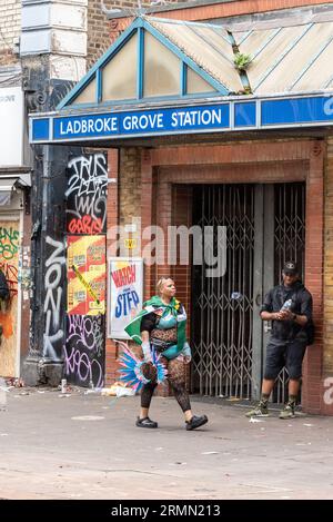 Person in Kostüm, die an der Ladbroke Grove Station bei der Notting Hill Carnival Grand Parade 2023 in London vorbeifährt. Eingang zur U-Bahn geschlossen Stockfoto