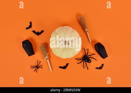 Halloween-Arrangement mit weißem Kürbis, schwarzen Spinnen, Fledermäusen und Särgen und Hexenbesen auf orangem Hintergrund Stockfoto