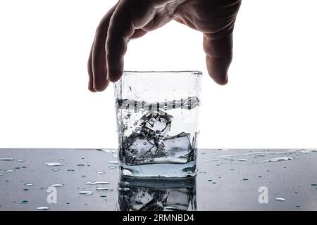 Hand, die ein Glas Eiswasser ergreift. Heller Hintergrund. Reflexion von Gläsern und Wassertropfen. Stockfoto