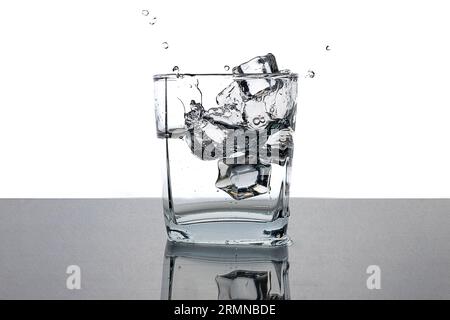 Kaltes Wasser in einem Glas mit Eiswürfeln. Wasserspritzer. Entspannen Sie sich an einem heißen Sommertag. Schwarzweißbild. Stockfoto