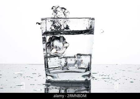 Kaltes Wasser in einem Glas mit Eiswürfeln. Wasserspritzer. Entspannen Sie sich an einem heißen Sommertag. Schwarzweißbild. Stockfoto