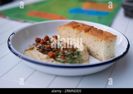 Ein Teller mit Hummus-Paste und ein Stück selbstgebackenes Brot wird am 25. August 2023 in einem Café in Warschau, Polen, mit Kichererbsen auf einem Tisch im Freien gesehen. Stockfoto