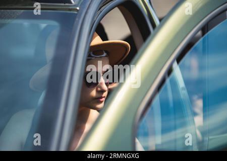 Porträt einer seriösen jungen Frau in einem Safarihut und Sonnenbrille, die ein Auto fährt Stockfoto