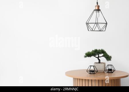 Couchtisch aus Holz mit Bonsaibaum und Kerzenständer in der Nähe der weißen Wand Stockfoto