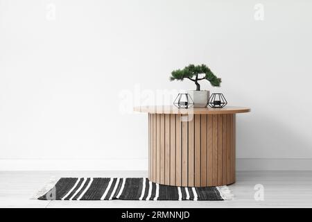 Couchtisch aus Holz mit Bonsaibaum und Kerzenständer in der Nähe der weißen Wand Stockfoto