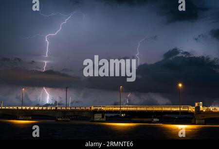 Himmel während eines schweren Sturms mit Donner und Blitz über dem Meer. Aufnahme einer Brücke mit vorbeifahrenden Autos, die eine Spur aus Licht erzeugen. Tornado kommt. Stockfoto