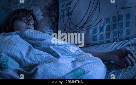 Die Schlafbrille der Frau trägt im Doppelbett am frühen Morgen oder bei Mondlicht Stockfoto