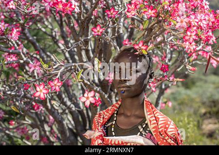 Das junge Mädchen des Stammes Larim steht in blauer Blüte in der Nähe des adeniumbaums Stockfoto