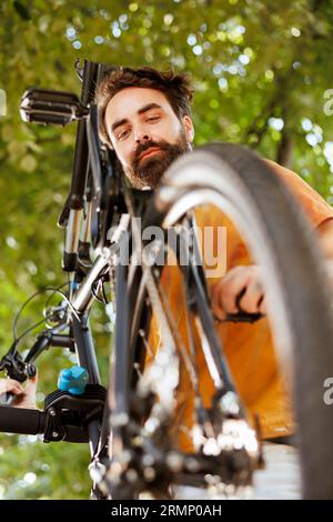 Gesunder lebendiger kaukasischer Mann wird im Freien gesehen, der jährliche Wartung und Wartung des modernen Fahrrads durchführt. Aktiver junger Radfahrer, der die Funktion des Fahrpedals überprüft und sicherstellt. Stockfoto