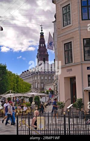 Blick auf Touristen, die auf der Fußgängerzone auf dem Amagertorv Platz gehen, vorbei an einer Terrasse und einem Café. Turm der Christen borg Palast im Hintergrund Stockfoto