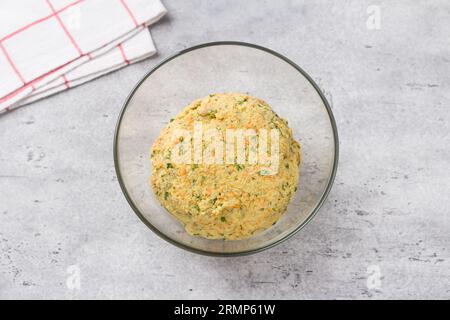 Teig für vegane Hirseschnitzel mit Karotten, Kräutern und Samen auf grauem strukturiertem Hintergrund, Draufsicht. Stufe des Kochens von gesunden hausgemachten Lebensmitteln. Stockfoto