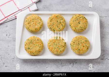 Rohe vegane Hirseschnitzel mit Karotten, Kräutern und Samen auf grauem strukturiertem Hintergrund, Draufsicht. Stufe des Kochens von gesunden hausgemachten Lebensmitteln. Stockfoto