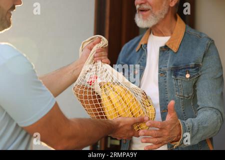 Mann mit Netztüte mit Produkten, die seinem älteren Nachbarn im Freien helfen, Nahaufnahme Stockfoto