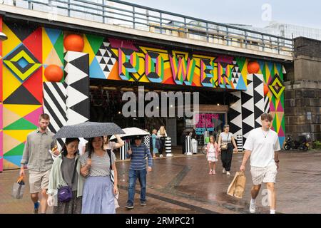 Menschen, die an einem regnerischen Tag in London durch den Eingang des Grosvenor Arch unter der Grosvenor Railway Bridge zum Battersea Power Station gehen. England Stockfoto