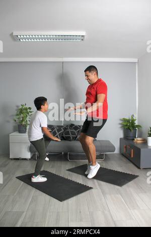 Latino Vater und Sohn haben gemeinsam in ihrem Wohnzimmer trainiert, um Gewicht zu verlieren und ihre Gesundheit zu verbessern Stockfoto