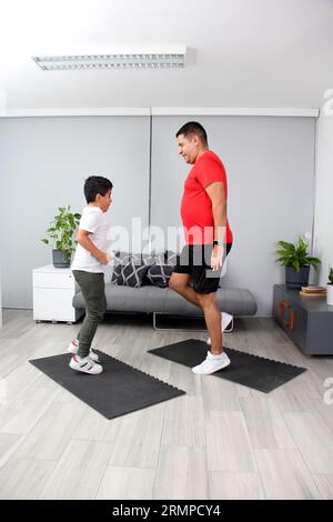 Latino Vater und Sohn haben gemeinsam in ihrem Wohnzimmer trainiert, um Gewicht zu verlieren und ihre Gesundheit zu verbessern Stockfoto