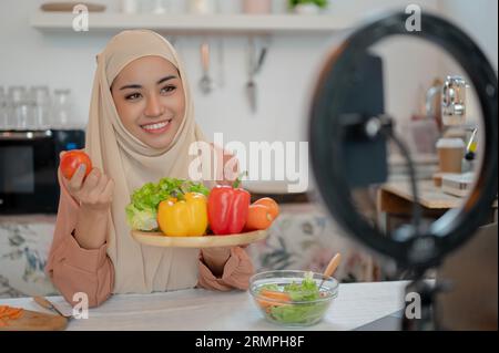 Eine wunderschöne asiatische muslimische Food-Bloggerin oder Lifestyle-Influencerin zeigt der Kamera die Zutaten ihrer gesunden Mahlzeit, während sie sie aufzeichnet Stockfoto