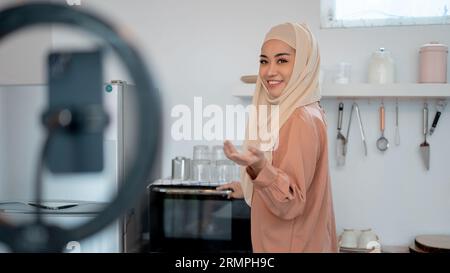 Eine wunderschöne asiatische muslimische Lifestyle-Influencerin oder Food-Bloggerin zeichnet ihr Video in der Küche auf und zeigt ihre Küchengeräte oder Werbung Stockfoto