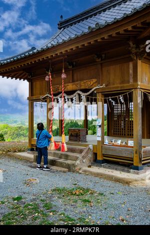 Japan, Kyushu. Shinto-Schrein auf dem Gelände von Oka Castle, Präfektur Oita. Frau, die Glocke klingelt, um der Gottheit im Heiligtum ihre Anwesenheit zu verkünden. Stockfoto