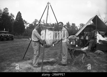 Beamte, die Tassen aus dem Beutel mit Flüssigkeit nachfüllen. Mitglieder der 114. Infanteriedivision der US-Armee trainieren im Zweiten Weltkrieg gegen Deutschland in Europa. Stockfoto