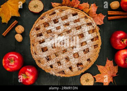 Hausgemachter Apfelkuchen, Äpfel, Nüsse, Zimt und Herbstblätter. Thanksgiving flach auf Holztisch gelegt. Stockfoto