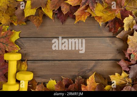 Kurzhanteln und Herbstlaub. Gesunde Fitness-Lifestyle-Zusammensetzung. Gym Workout Sport Training Flat-Lay mit Kopierraum auf Holzuntergrund. Stockfoto