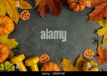 Kurzhanteln und Halloween-Deko, herbstliche Kürbisse, Herbstblätter. Fitnesskomposition, Fitness-Workout, Sporttraining, flaches Lay-Konzept mit Kopierbereich. Stockfoto