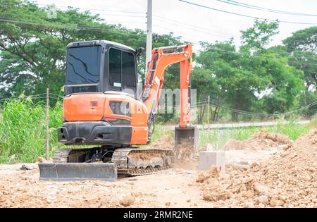 Arbeiter, der einen Minibagger benutzt, um ein Loch aus Fundamentstapel auf der Baustelle zu bedecken. Stockfoto