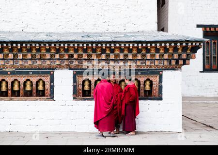 Punakha, Bhutan - 03. Dezember 2018: Drei buddhistische Studentenmönche stehen an den religiösen Gebetsrädern im Kloster Chimi Lhakang, Punakha, Bhutan Stockfoto