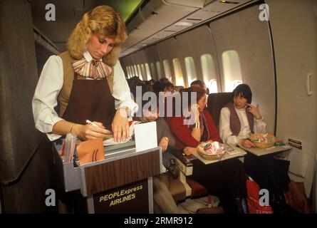 People Express PeoplExpress Airline, 26. Mai 1983 erster Flug Flughafen Gatwick London nach Newark, New Jersey USA. Stewardess in der Flugbegleitung nimmt Zahlungen von $149 für ein an Bord des Flugzeugs gekauftes One-Way-Ticket entgegen. 1980er Jahre HOMER SYKES Stockfoto