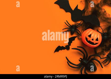 Halloween Konzept Hintergrund. Ansicht von oben auf Kürbiskorb, Spinnen und Fledermäuse mit Platz für Text auf orangem Hintergrund. Halloween Party Dekoration Konz Stockfoto