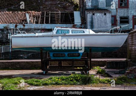 Eine alte Yacht sitzt an einem sonnigen Tag auf der Wiege aus dem Wasser vor einigen alten verlassenen Gebäuden in Pennan, Aberdeenshire, Schottland. Stockfoto