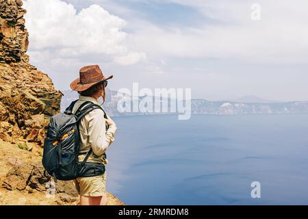 Eine Frau mit einem Rucksack in Hut auf dem Hügel mit Blick auf einen malerischen See Stockfoto