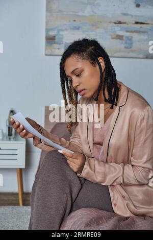 afroamerikanische Frau, die Ultraschallfoto betrachtet, Schwangerschaft, Entscheidung trifft, modernes Schlafzimmer Stockfoto