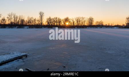 Sonnenuntergang über dem gefrorenen Teich mit Bäumen am Ufer während des Wintertages mit klarem Himmel im Park Bozeny Nemcove in der Stadt Karvina in tschechien Stockfoto