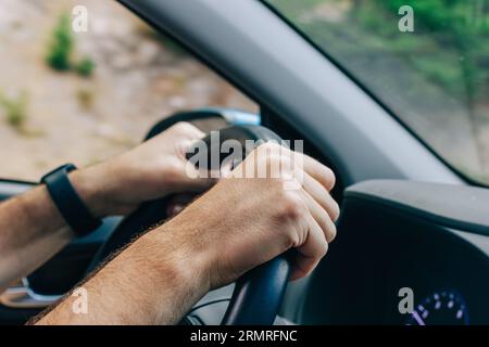 Nahaufnahme der männlichen Hände am Lenkrad, Roadtrip, Blick von der Innenseite des Fahrzeugs Stockfoto