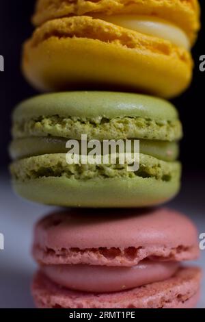 Macarons in gelben, rosa und grünen Farben auf schwarzem Hintergrund, Nahaufnahme. Stockfoto